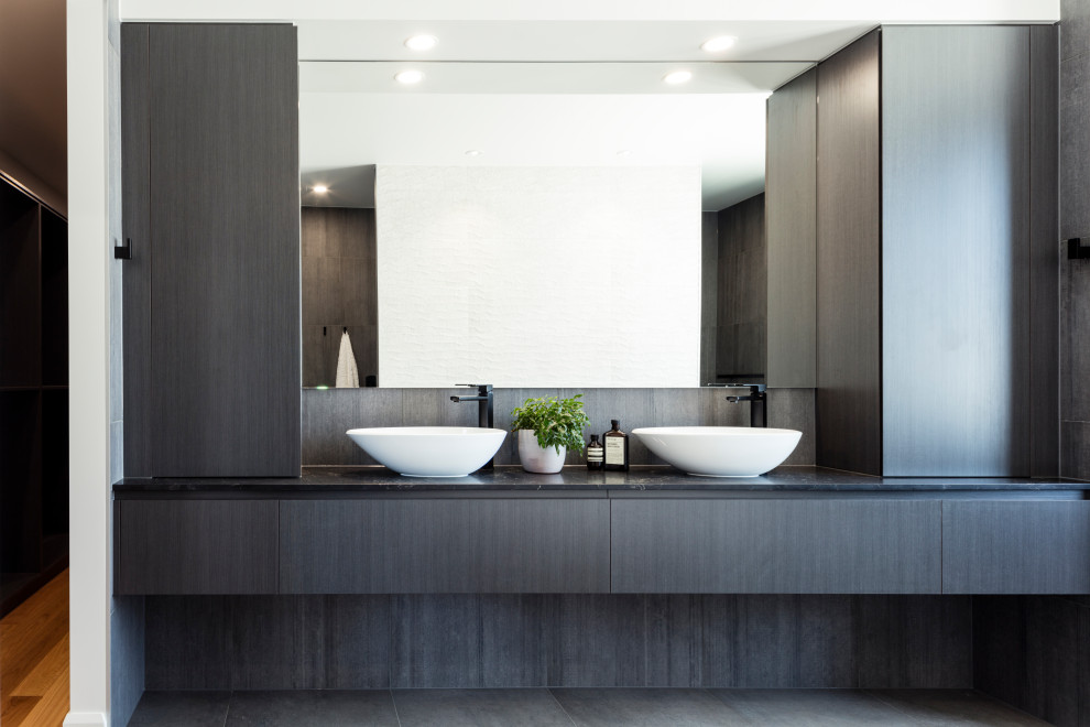 This is an example of a modern master bathroom in Sunshine Coast with dark wood cabinets, a freestanding tub, cement tiles, a vessel sink, black floor, black benchtops, a single vanity and a floating vanity.