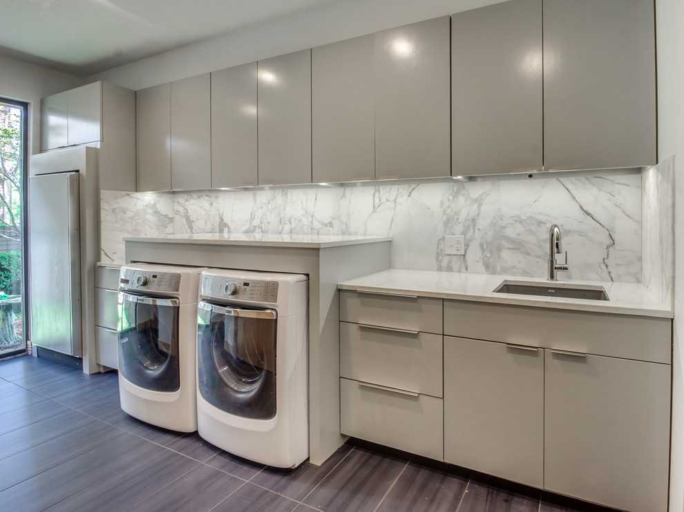 Inspiration for a large modern single-wall utility room in Oklahoma City with an undermount sink, flat-panel cabinets, grey cabinets, marble benchtops, grey walls, laminate floors, a side-by-side washer and dryer and brown floor.