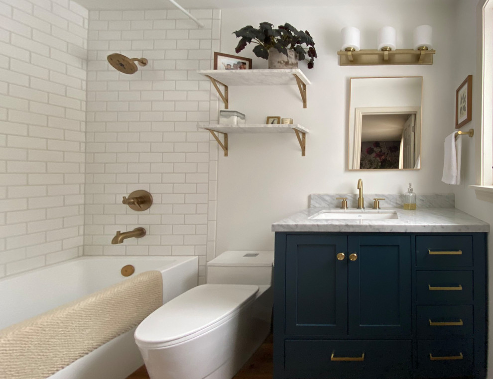 Пример оригинального дизайна: маленькая главная ванная комната в стиле неоклассика (современная классика) с фасадами в стиле шейкер, синими фасадами, ванной в нише, душем в нише, унитазом-моноблоком, белой плиткой, керамогранитной плиткой, белыми стенами, полом из винила, врезной раковиной, мраморной столешницей, коричневым полом, шторкой для ванной, белой столешницей, тумбой под одну раковину и напольной тумбой для на участке и в саду