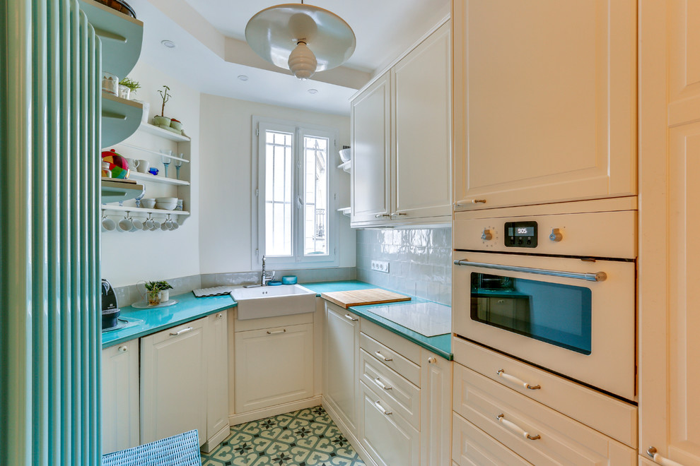 Inspiration for a transitional u-shaped kitchen in Paris with a farmhouse sink, raised-panel cabinets, white cabinets, grey splashback, subway tile splashback, white appliances, no island, multi-coloured floor and turquoise benchtop.