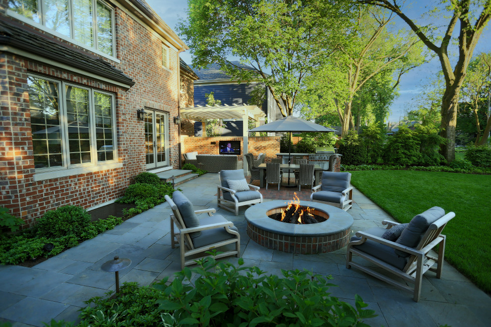 Example of a mid-sized classic backyard stone patio design in Chicago with a fire pit and a pergola