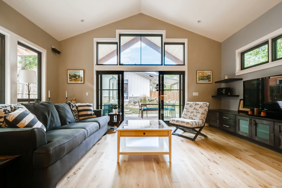Cette image montre une salle de séjour design de taille moyenne et ouverte avec un mur beige, parquet clair, un manteau de cheminée en pierre de parement, un téléviseur indépendant, un sol marron et poutres apparentes.