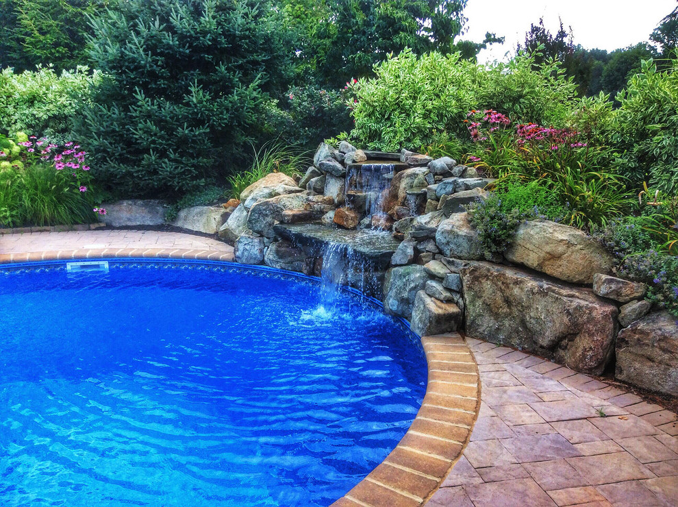 Large traditional backyard kidney-shaped natural pool in New York with a water feature and concrete pavers.