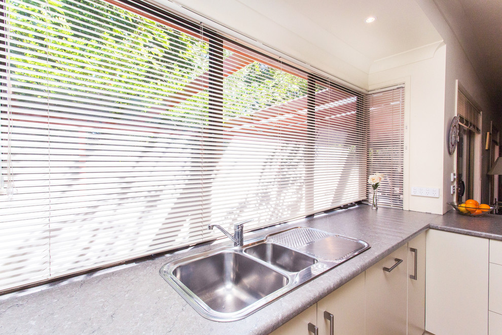 Mid-sized contemporary u-shaped eat-in kitchen in Other with a drop-in sink, flat-panel cabinets, white cabinets, laminate benchtops, grey splashback, ceramic splashback, stainless steel appliances, ceramic floors, a peninsula, brown floor and grey benchtop.