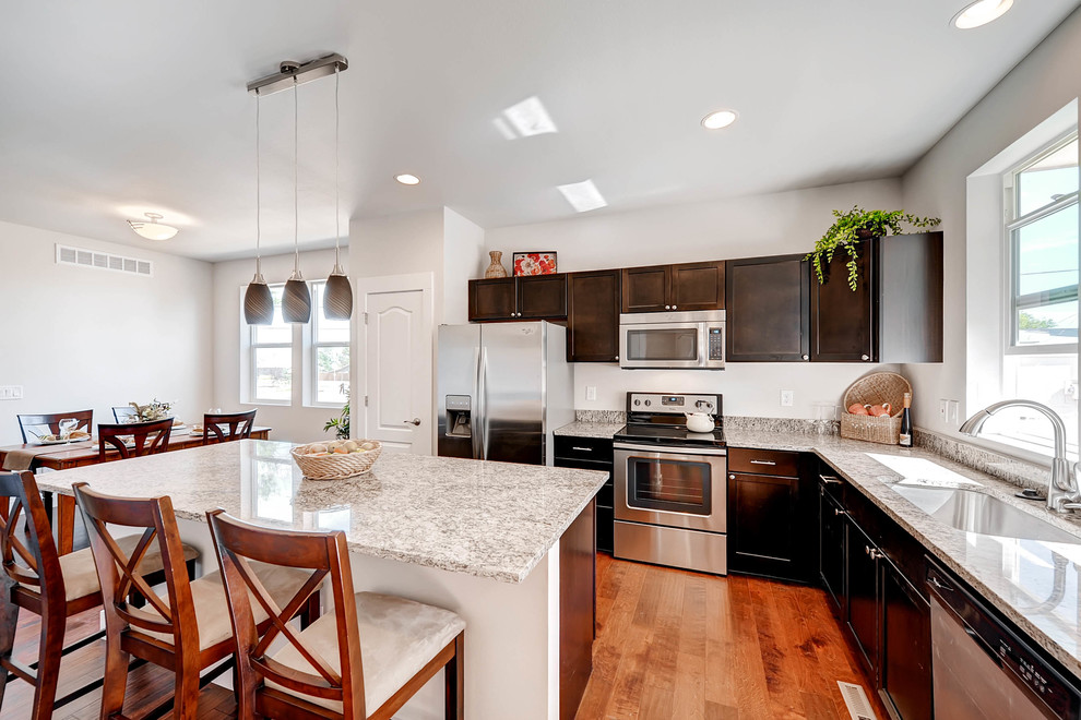 Example of a medium tone wood floor and brown floor kitchen design in Denver with an undermount sink, shaker cabinets, dark wood cabinets, granite countertops, stainless steel appliances and an island