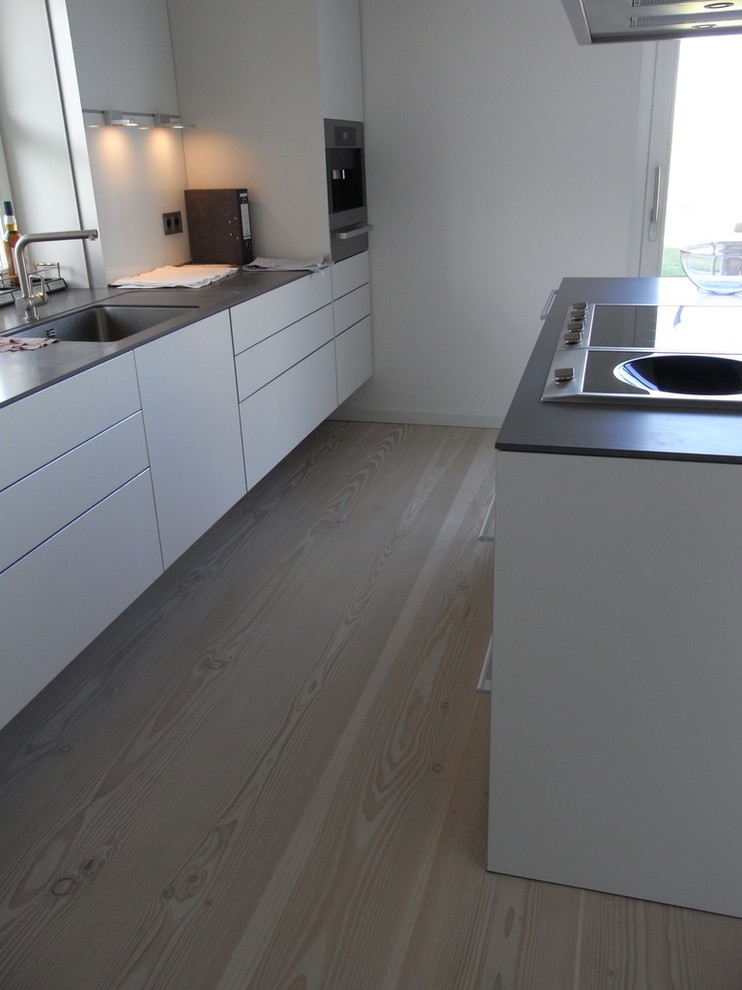 Inspiration for a mid-sized scandinavian galley open plan kitchen in Berlin with an integrated sink, flat-panel cabinets, light wood cabinets, limestone benchtops, white splashback, ceramic splashback, stainless steel appliances, light hardwood floors and with island.