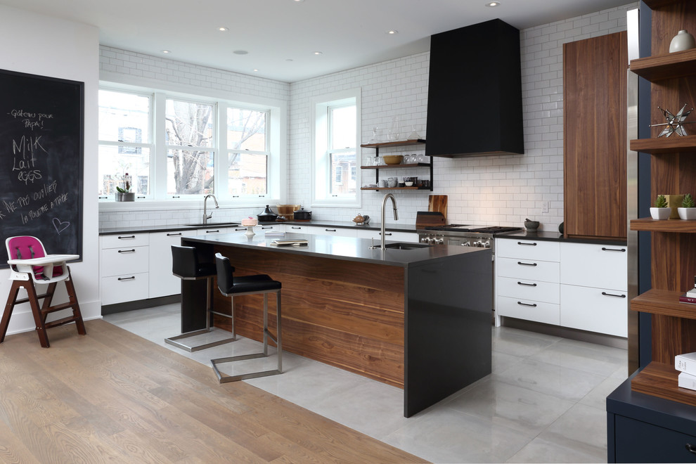 This is an example of a contemporary l-shaped kitchen in Montreal with an undermount sink, flat-panel cabinets, white splashback, subway tile splashback, stainless steel appliances and with island.