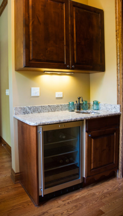 Example of a small transitional single-wall medium tone wood floor and brown floor wet bar design in Chicago with an undermount sink, raised-panel cabinets, medium tone wood cabinets and granite countertops