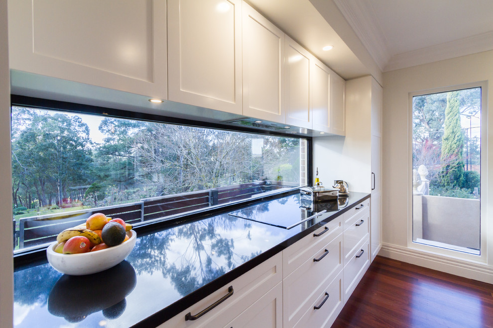Large contemporary u-shaped eat-in kitchen in Melbourne with an undermount sink, shaker cabinets, white cabinets, marble benchtops, white splashback, window splashback, black appliances, dark hardwood floors, with island, brown floor and white benchtop.