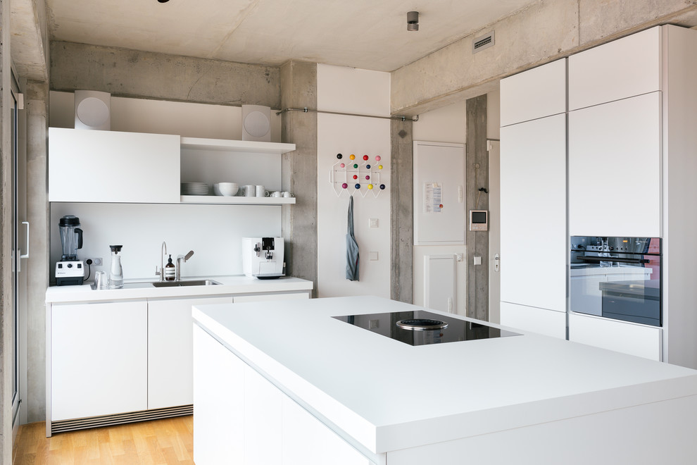 Design ideas for an industrial galley separate kitchen in Berlin with a drop-in sink, flat-panel cabinets, white cabinets, white splashback, black appliances, medium hardwood floors and with island.