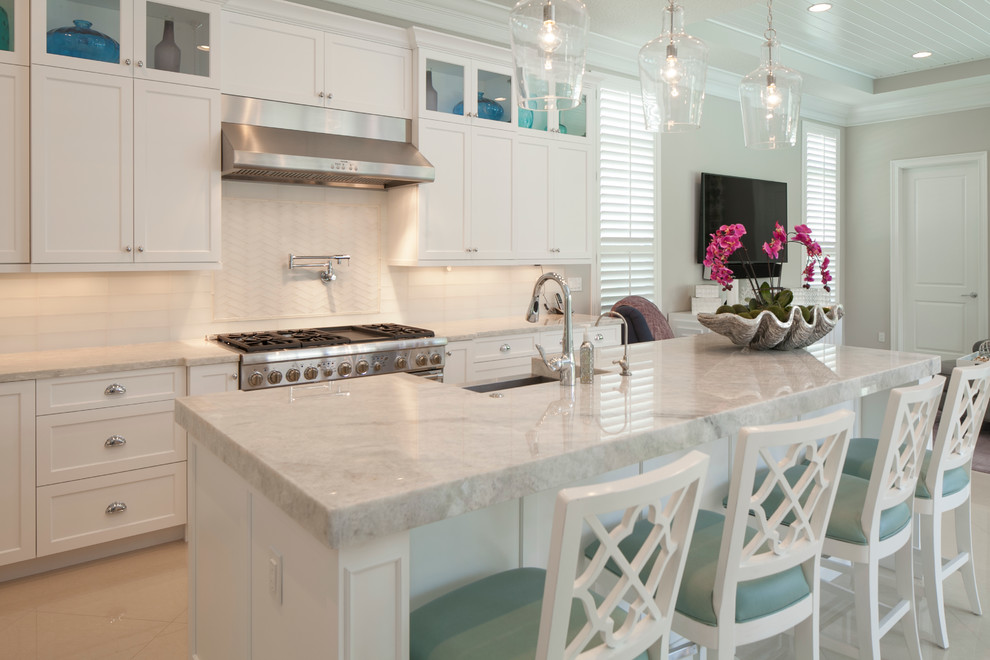 Large transitional l-shaped open plan kitchen in Miami with white splashback, with island, a farmhouse sink, shaker cabinets, white cabinets, marble benchtops, porcelain splashback, stainless steel appliances, marble floors and beige floor.
