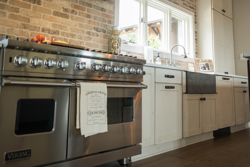 Large transitional galley dark wood floor and brown floor open concept kitchen photo with a farmhouse sink, shaker cabinets, quartz countertops, brown backsplash, brick backsplash, stainless steel appliances and an island