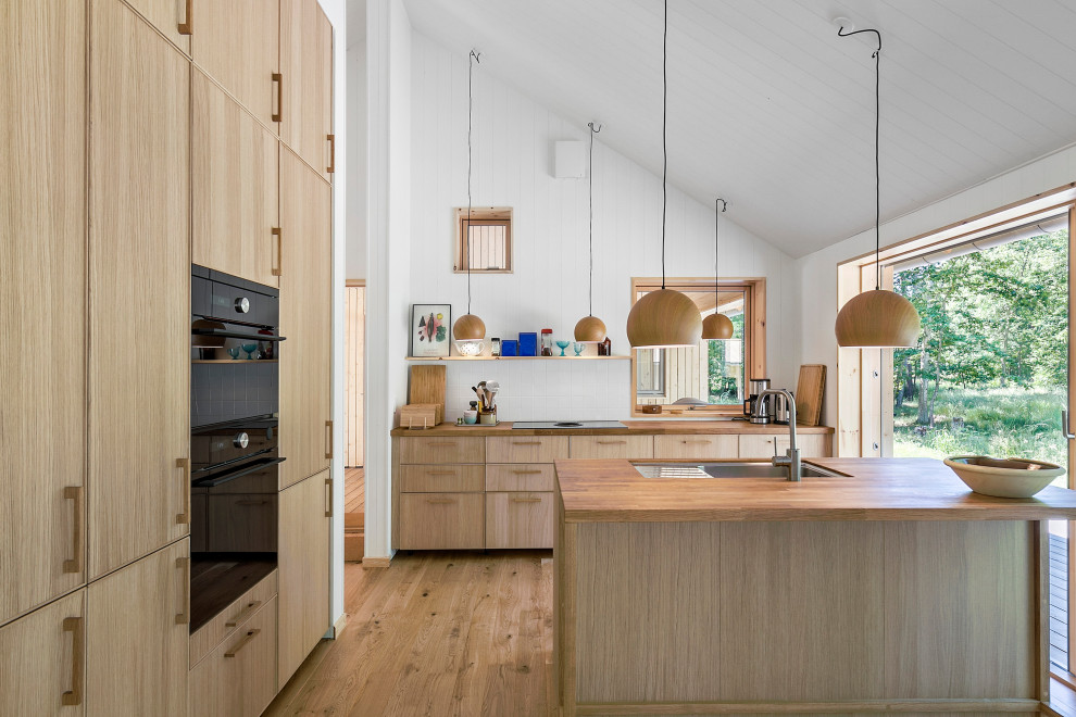 Photo of a scandinavian u-shaped separate kitchen in Copenhagen with a drop-in sink, recessed-panel cabinets, medium wood cabinets, wood benchtops, white splashback, panelled appliances, medium hardwood floors, with island, brown floor, brown benchtop, timber and vaulted.