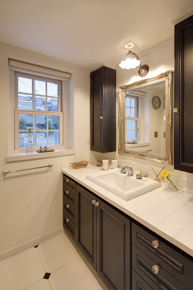 Design ideas for a traditional powder room in Other with recessed-panel cabinets, dark wood cabinets, white walls, a drop-in sink and tile benchtops.