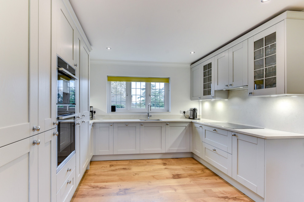 Exempel på ett stort modernt vit vitt kök, med en undermonterad diskho, skåp i shakerstil, grå skåp, bänkskiva i kvartsit, vitt stänkskydd, integrerade vitvaror, mellanmörkt trägolv, en köksö och brunt golv