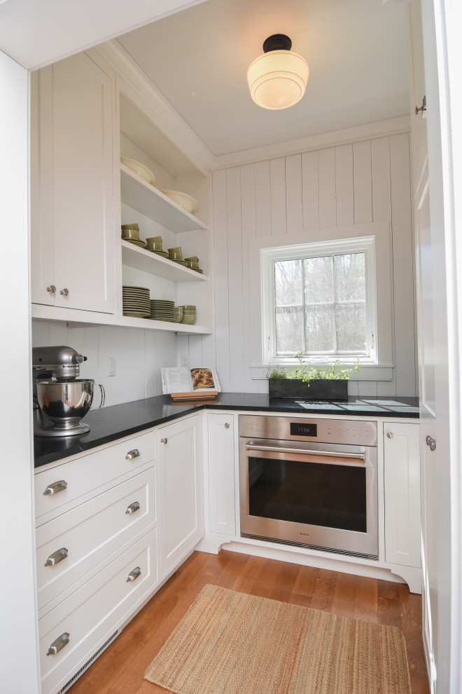 Country Küche in U-Form mit Vorratsschrank, Schrankfronten im Shaker-Stil, weißen Schränken, Rückwand aus Holzdielen, hellem Holzboden und schwarzer Arbeitsplatte in Boston