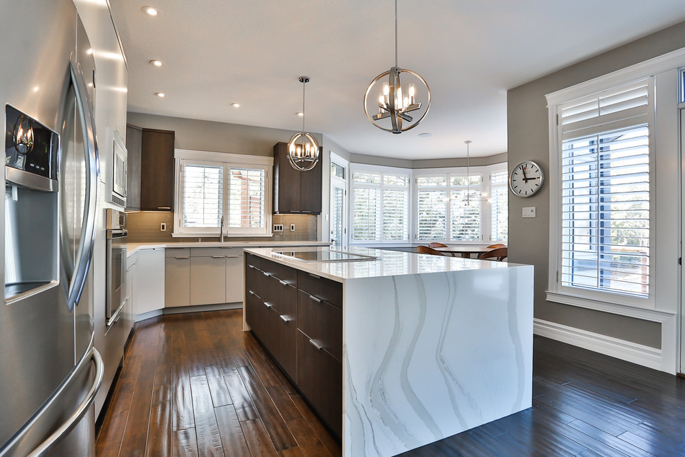 Large contemporary l-shaped eat-in kitchen in Toronto with a double-bowl sink, flat-panel cabinets, grey cabinets, quartz benchtops, grey splashback, glass tile splashback, stainless steel appliances, medium hardwood floors, with island, brown floor and white benchtop.