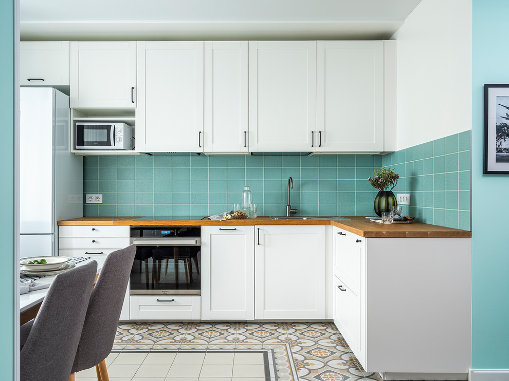 Contemporary l-shaped eat-in kitchen in Moscow with shaker cabinets, white cabinets, wood benchtops, no island, brown benchtop, a drop-in sink, blue splashback, white appliances and multi-coloured floor.