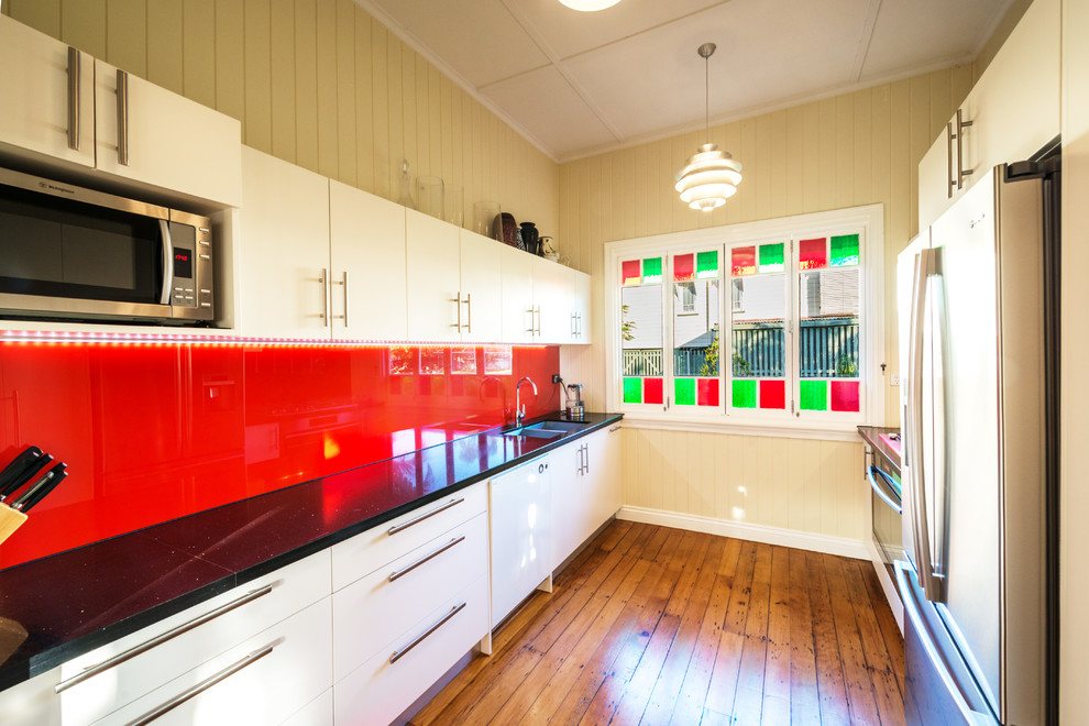 Photo of a transitional galley kitchen pantry in Brisbane with a double-bowl sink, flat-panel cabinets, white cabinets, quartz benchtops, red splashback, glass sheet splashback, stainless steel appliances, light hardwood floors and no island.