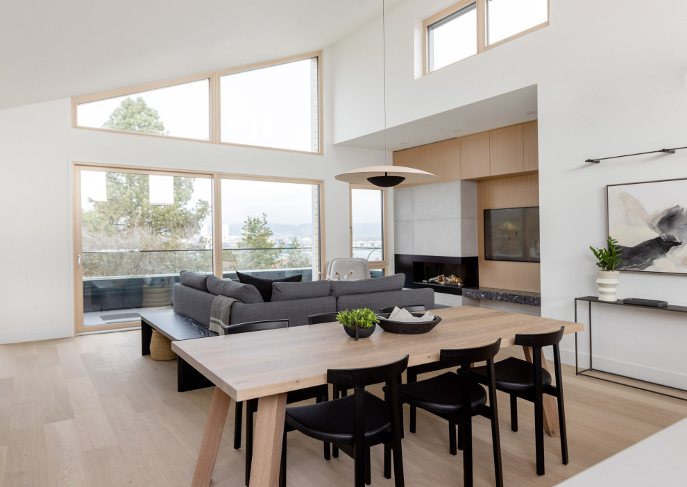 Design ideas for a medium sized scandi open plan dining room in Vancouver with white walls, light hardwood flooring, a hanging fireplace, a concrete fireplace surround and beige floors.