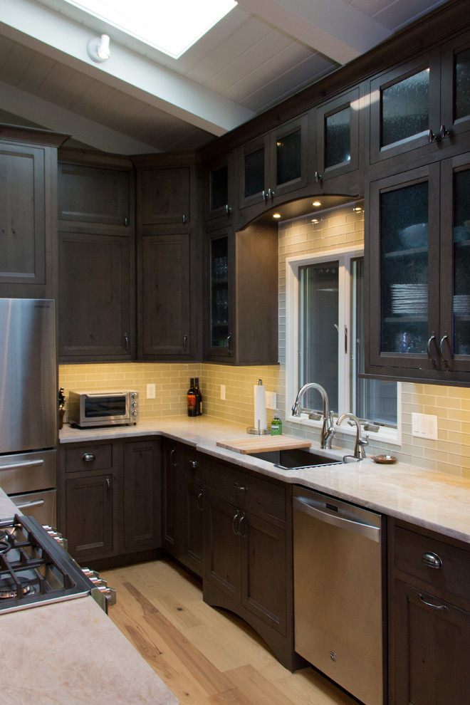 Mid-sized transitional l-shaped light wood floor eat-in kitchen photo with an undermount sink, recessed-panel cabinets, dark wood cabinets, onyx countertops, gray backsplash, glass tile backsplash, stainless steel appliances and an island