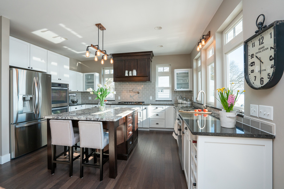 Large transitional u-shaped kitchen in Detroit with a double-bowl sink, flat-panel cabinets, white cabinets, granite benchtops, grey splashback, ceramic splashback, stainless steel appliances, dark hardwood floors, with island, brown floor and multi-coloured benchtop.