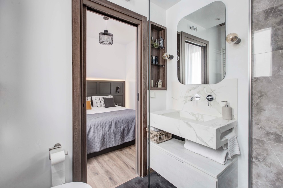 Photo of a small industrial master bathroom in Madrid with a corner shower, a wall-mount toilet, gray tile, white walls, ceramic floors, a trough sink, engineered quartz benchtops, black floor and an open shower.