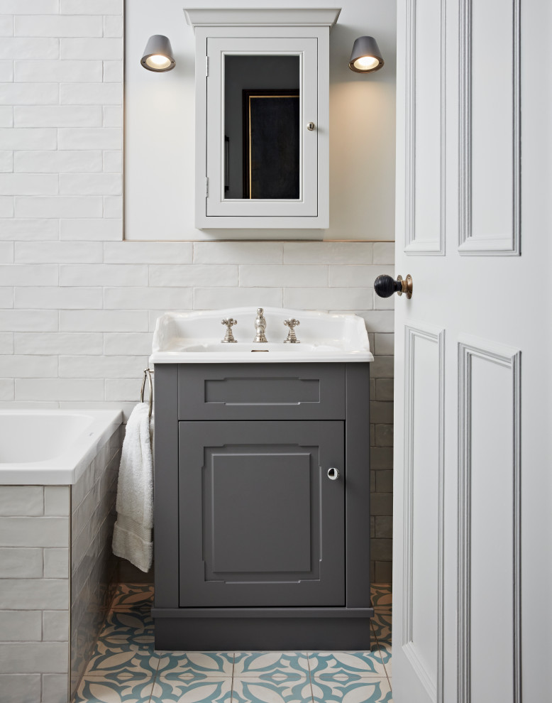 This is an example of a small classic family bathroom in London with recessed-panel cabinets, grey cabinets, a built-in bath, a shower/bath combination, a two-piece toilet, white tiles, marble tiles, cement flooring, an integrated sink, blue floors, a single sink and a freestanding vanity unit.