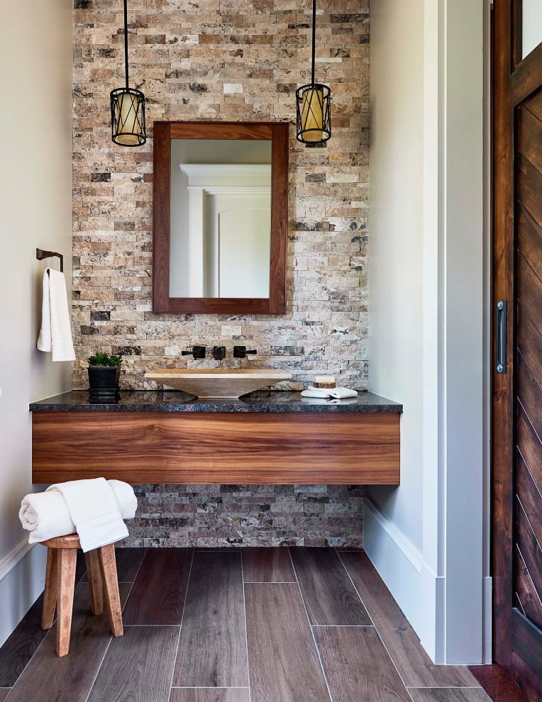 Inspiration for a country bathroom in Raleigh with medium wood cabinets, multi-coloured tile, beige walls, a vessel sink, brown floor and black benchtops.