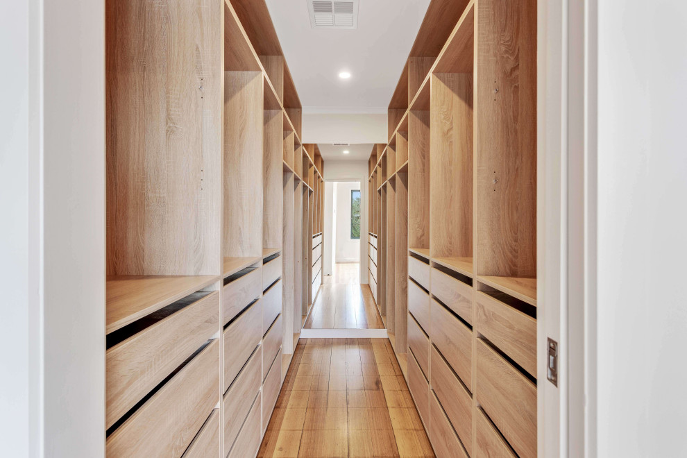 Large modern walk-in wardrobe in Melbourne with light wood cabinets, light hardwood floors and brown floor.
