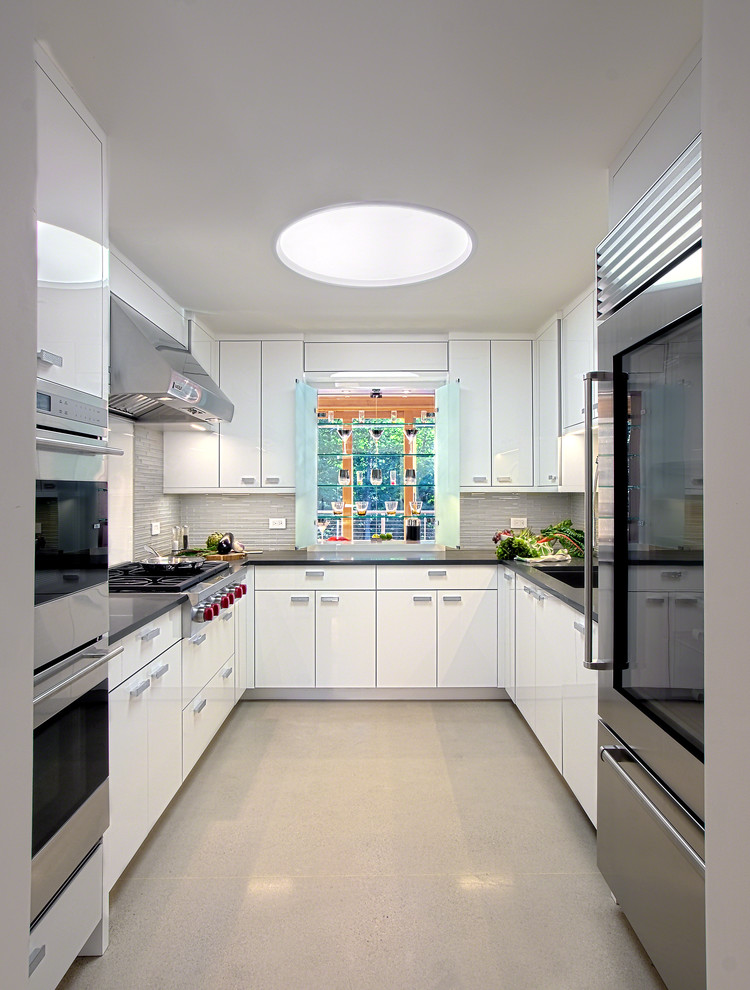 This is an example of a small contemporary u-shaped eat-in kitchen in Milwaukee with an undermount sink, flat-panel cabinets, white cabinets, grey splashback, stainless steel appliances, no island, quartzite benchtops, glass tile splashback, concrete floors, beige floor and brown benchtop.