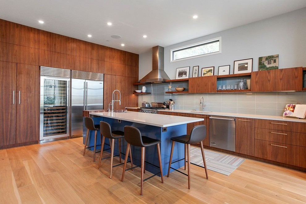 This is an example of a mid-sized contemporary l-shaped eat-in kitchen in San Francisco with an undermount sink, flat-panel cabinets, solid surface benchtops, grey splashback, porcelain splashback, stainless steel appliances, light hardwood floors, with island and medium wood cabinets.