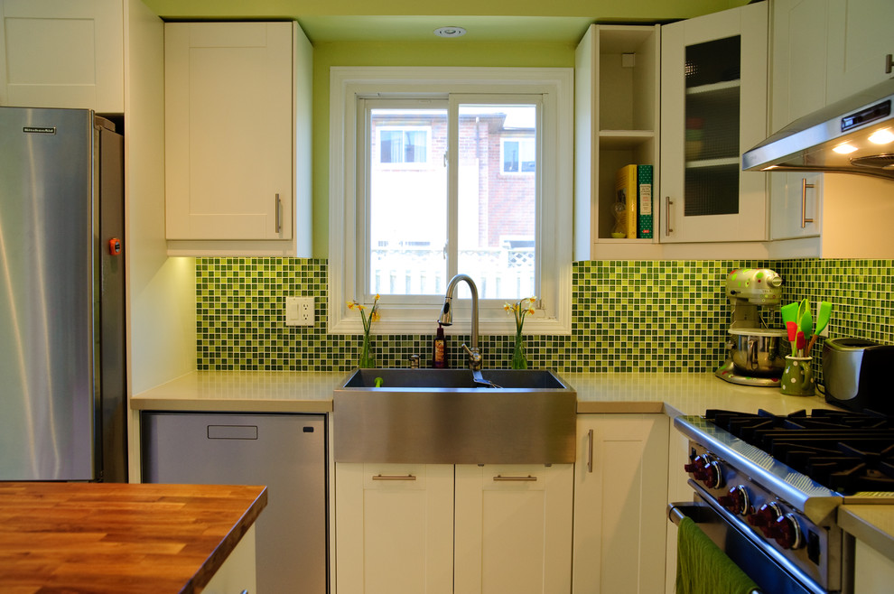 Contemporary l-shaped kitchen in Toronto with a farmhouse sink, shaker cabinets, green splashback, mosaic tile splashback and stainless steel appliances.