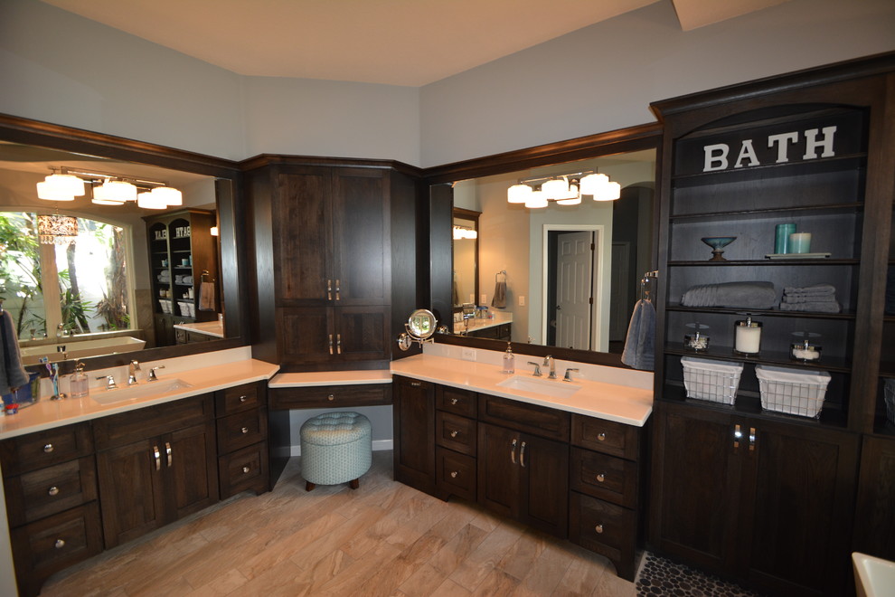 This is an example of a large transitional master bathroom in Tampa with shaker cabinets, dark wood cabinets, a freestanding tub, a curbless shower, a one-piece toilet, gray tile, porcelain tile, pebble tile floors, an undermount sink and engineered quartz benchtops.