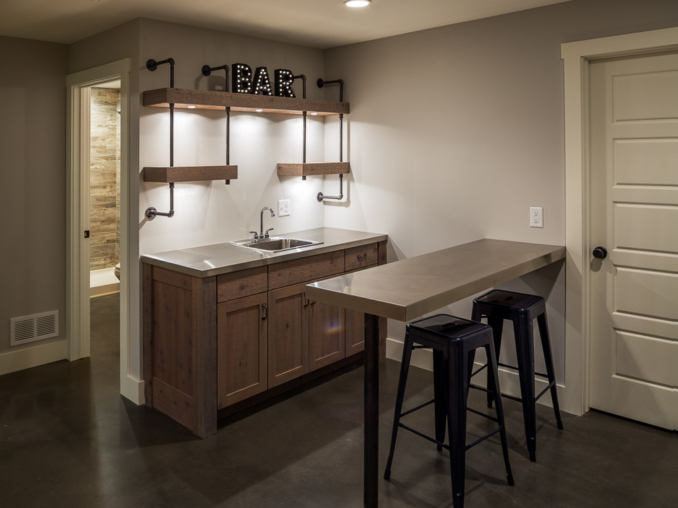 This is an example of a mid-sized country single-wall wet bar in Minneapolis with a drop-in sink, shaker cabinets, distressed cabinets, stainless steel benchtops, concrete floors and grey floor.