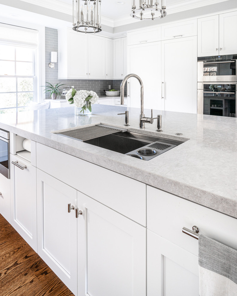 Inspiration for a large classic u-shaped kitchen/diner in Philadelphia with a submerged sink, shaker cabinets, white cabinets, engineered stone countertops, grey splashback, glass tiled splashback, integrated appliances, dark hardwood flooring, an island, brown floors and white worktops.