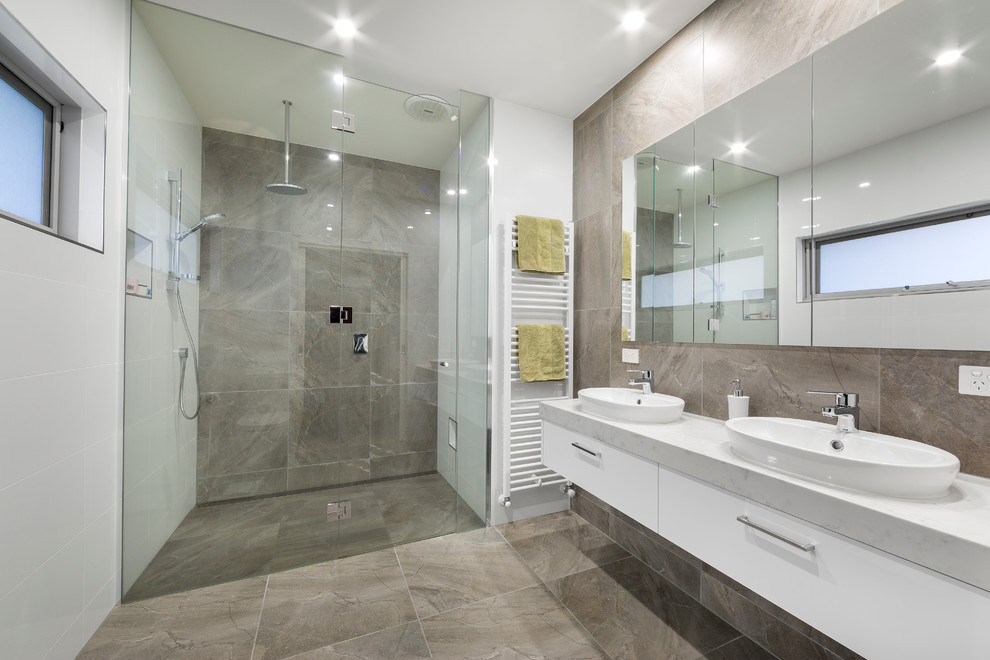 Photo of a large contemporary master bathroom in Melbourne with flat-panel cabinets, white cabinets, a curbless shower, white walls, a vessel sink, gray tile, a hinged shower door, travertine, travertine floors, marble benchtops and grey floor.