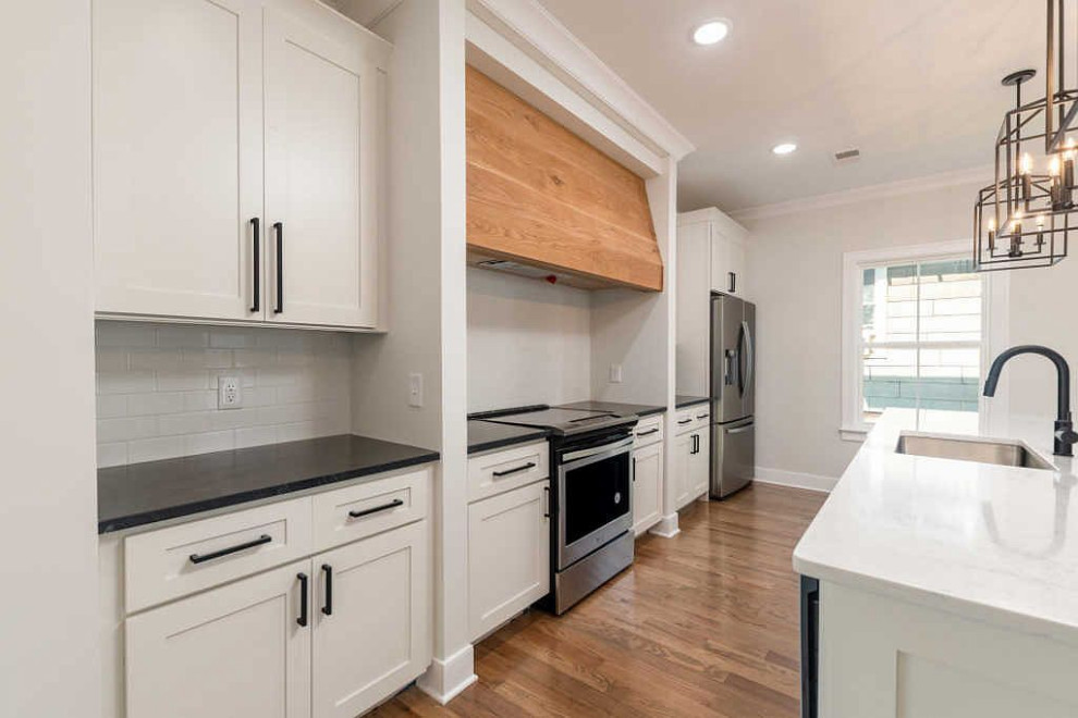 Open concept kitchen - large transitional galley medium tone wood floor and brown floor open concept kitchen idea with an undermount sink, shaker cabinets, white cabinets, quartz countertops, white backsplash, ceramic backsplash, stainless steel appliances, an island and white countertops