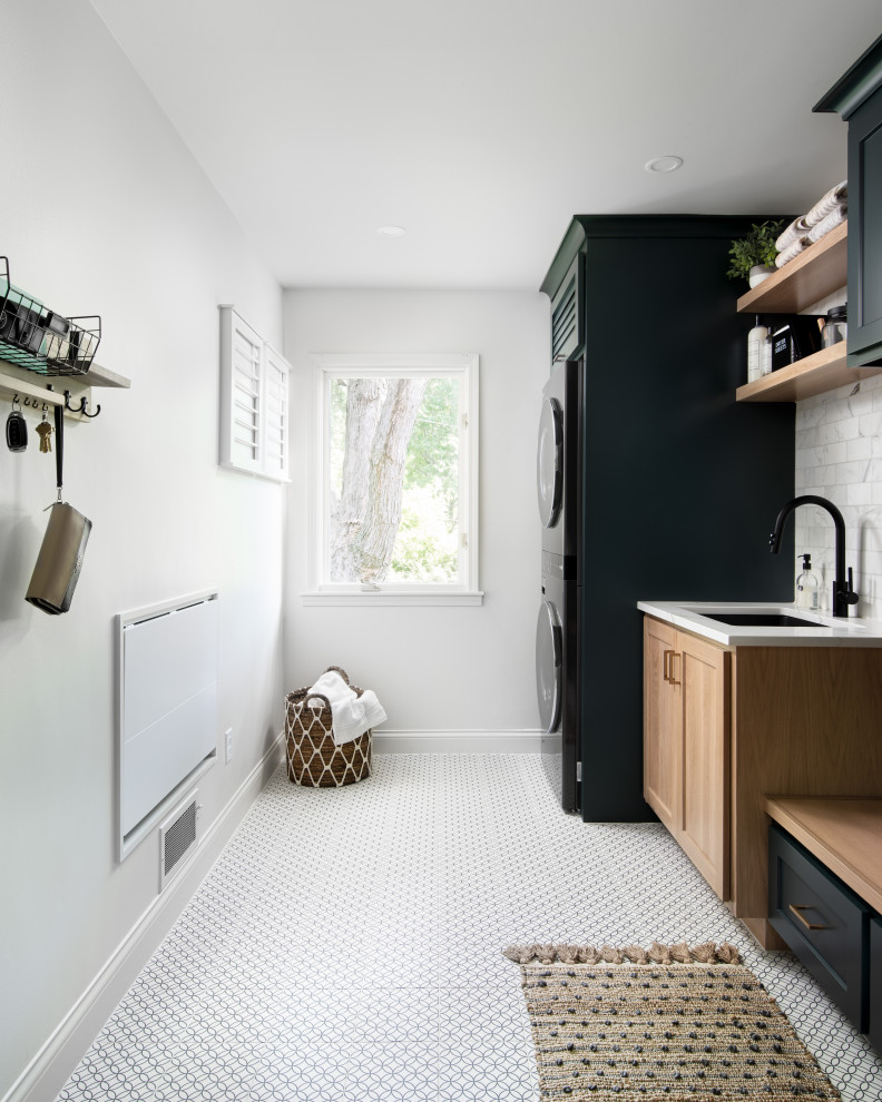 Example of a mid-sized transitional single-wall porcelain tile and white floor dedicated laundry room design in Kansas City with an undermount sink, recessed-panel cabinets, green cabinets, quartz countertops, white backsplash, marble backsplash, white walls, a stacked washer/dryer and white countertops