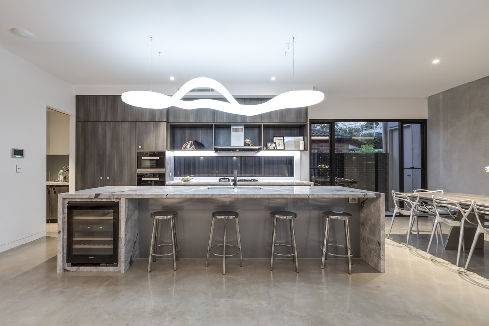 This is an example of a mid-sized modern galley kitchen pantry in Brisbane with an undermount sink, beaded inset cabinets, medium wood cabinets, marble benchtops, glass sheet splashback, black appliances, concrete floors, with island and beige floor.