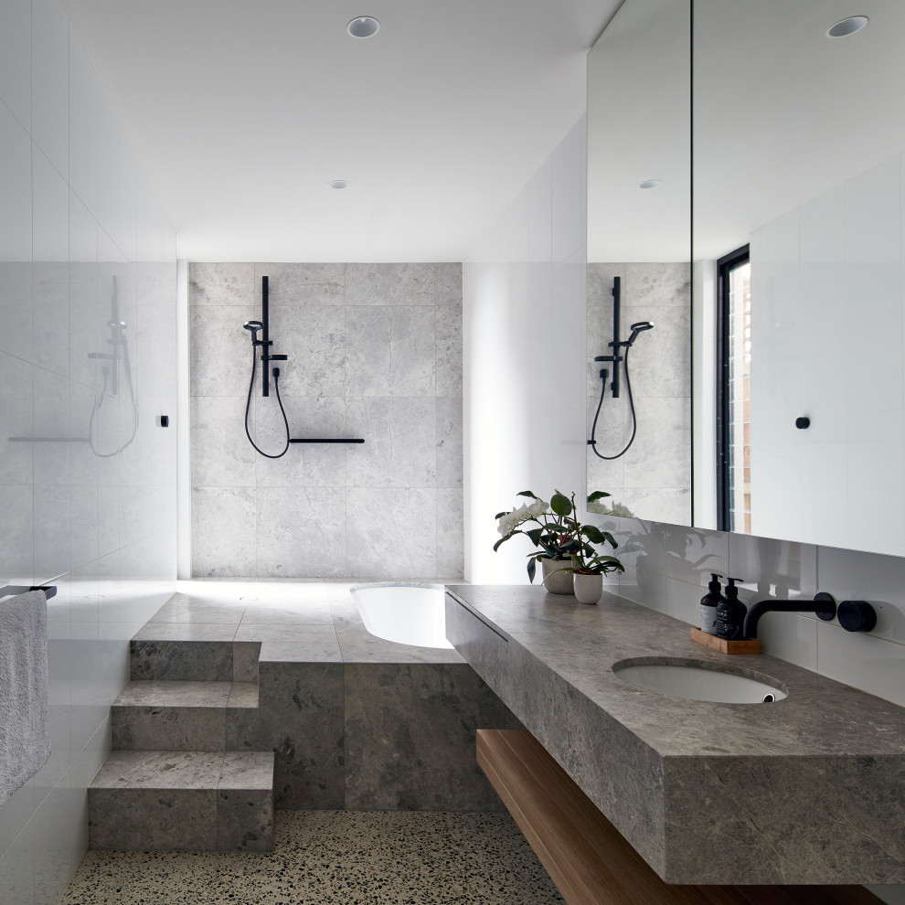 Mid-sized contemporary bathroom in Melbourne with flat-panel cabinets, an undermount tub, white tile, ceramic tile, white walls, limestone floors, an undermount sink, limestone benchtops, grey floor, an open shower, grey benchtops and a curbless shower.