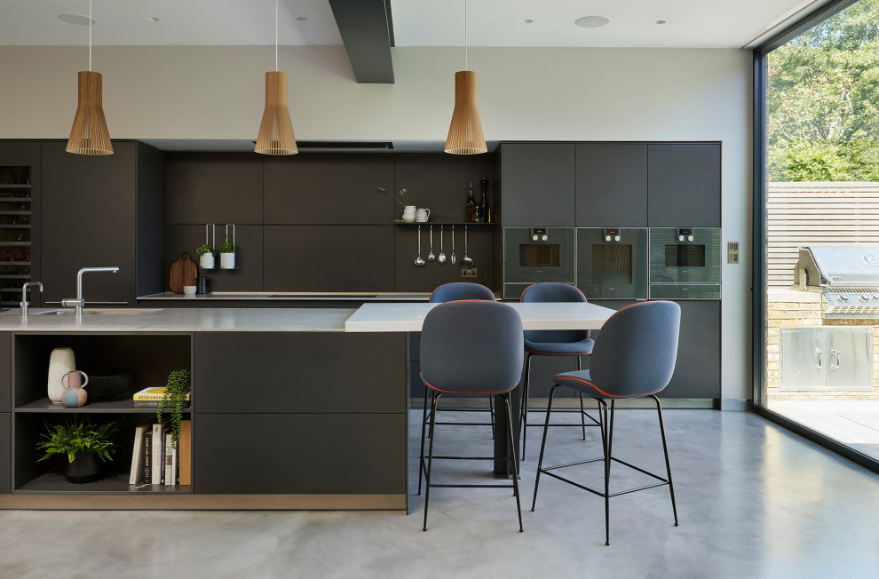 Inspiration for a contemporary grey and white open plan kitchen in Other with a built-in sink, flat-panel cabinets, grey cabinets, marble worktops, white splashback, marble splashback, black appliances, concrete flooring, an island, grey floors and white worktops.