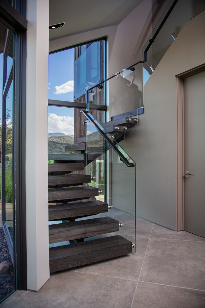 This is an example of a large contemporary wood curved staircase in Denver with open risers and glass railing.