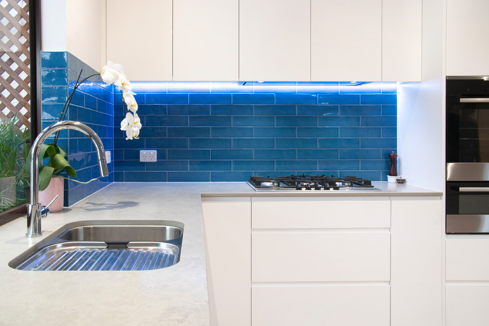 Inspiration for a mid-sized contemporary l-shaped open plan kitchen in Newcastle - Maitland with an undermount sink, flat-panel cabinets, white cabinets, quartz benchtops, blue splashback, subway tile splashback, stainless steel appliances, light hardwood floors, with island and grey benchtop.