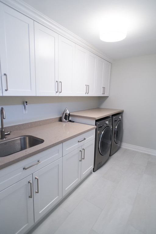 Inspiration for a mid-sized transitional galley dedicated laundry room in Toronto with an undermount sink, shaker cabinets, white cabinets, quartz benchtops, grey walls, ceramic floors and a side-by-side washer and dryer.