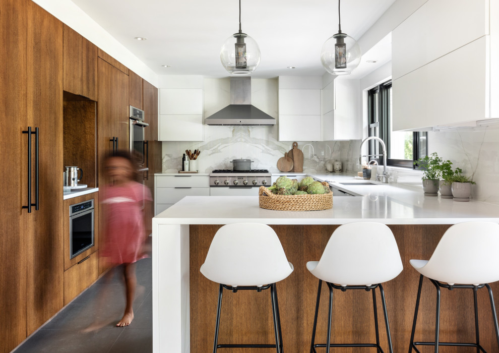 Large contemporary l-shaped enclosed kitchen in New York with a submerged sink, flat-panel cabinets, white cabinets, engineered stone countertops, white splashback, glass sheet splashback, stainless steel appliances, porcelain flooring, a breakfast bar, black floors and white worktops.