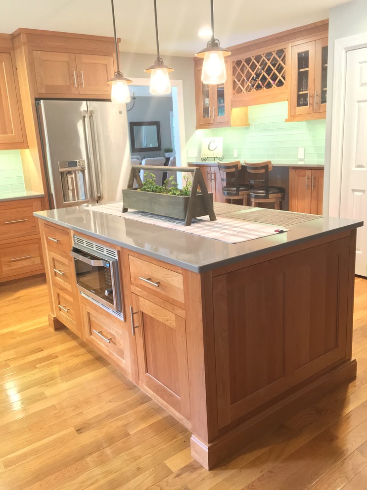 This is an example of a mid-sized transitional l-shaped kitchen in Atlanta with a farmhouse sink, shaker cabinets, light wood cabinets, quartz benchtops, green splashback, glass tile splashback, stainless steel appliances, medium hardwood floors and with island.