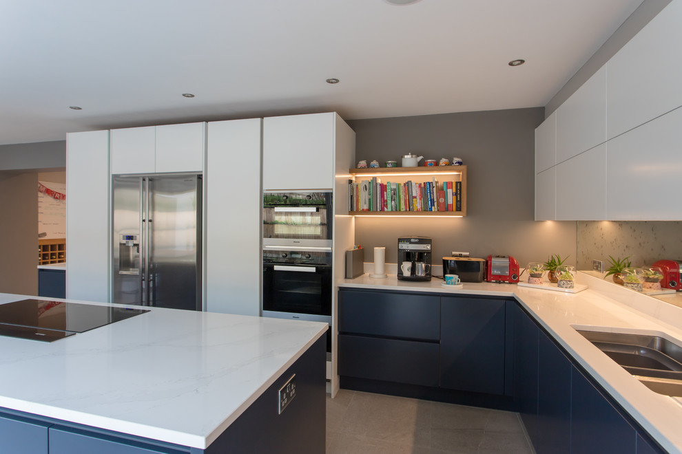 This is an example of an expansive contemporary l-shaped eat-in kitchen in Hertfordshire with a drop-in sink, flat-panel cabinets, blue cabinets, quartzite benchtops, metallic splashback, mirror splashback, stainless steel appliances, porcelain floors, with island, white floor and white benchtop.