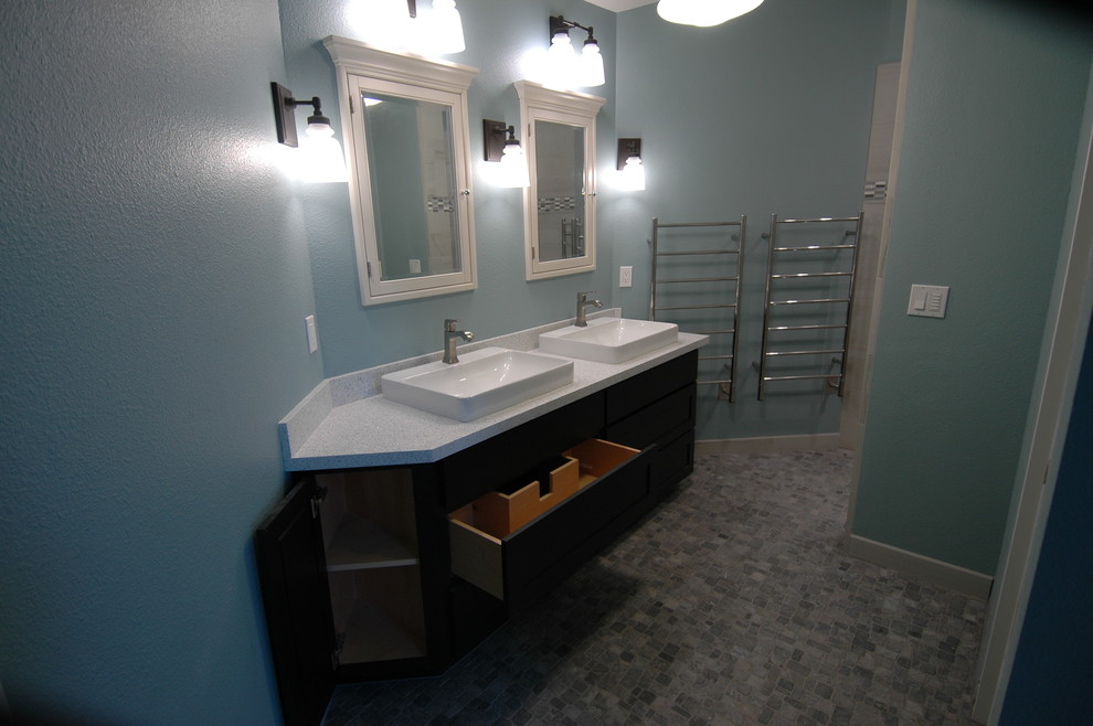 This is an example of a mid-sized contemporary master bathroom in Sacramento with recessed-panel cabinets, black cabinets, a curbless shower, a wall-mount toilet, multi-coloured tile, porcelain tile, blue walls, pebble tile floors, a vessel sink and recycled glass benchtops.