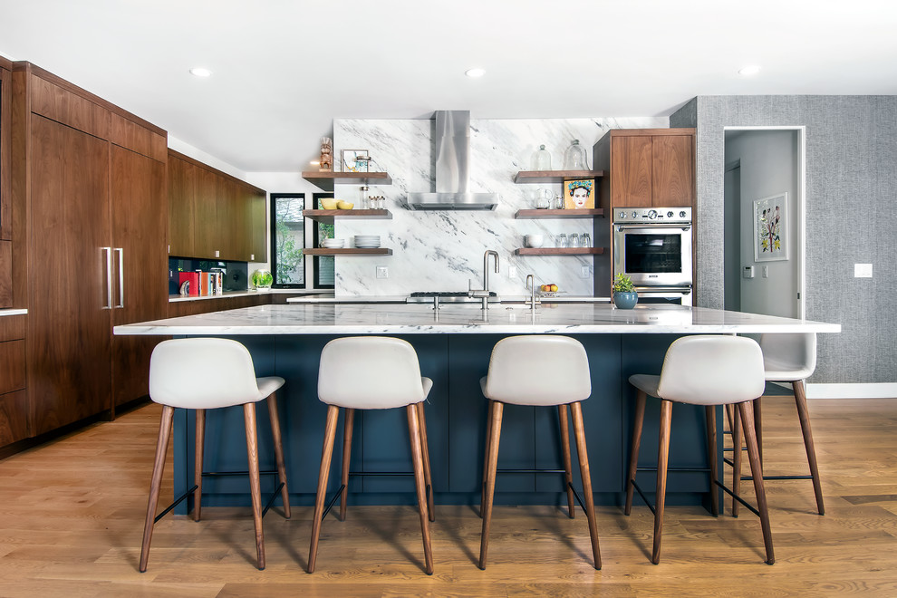 This is an example of a midcentury kitchen in Denver with flat-panel cabinets, dark wood cabinets, marble benchtops, white splashback, marble splashback, panelled appliances, medium hardwood floors, with island and white benchtop.